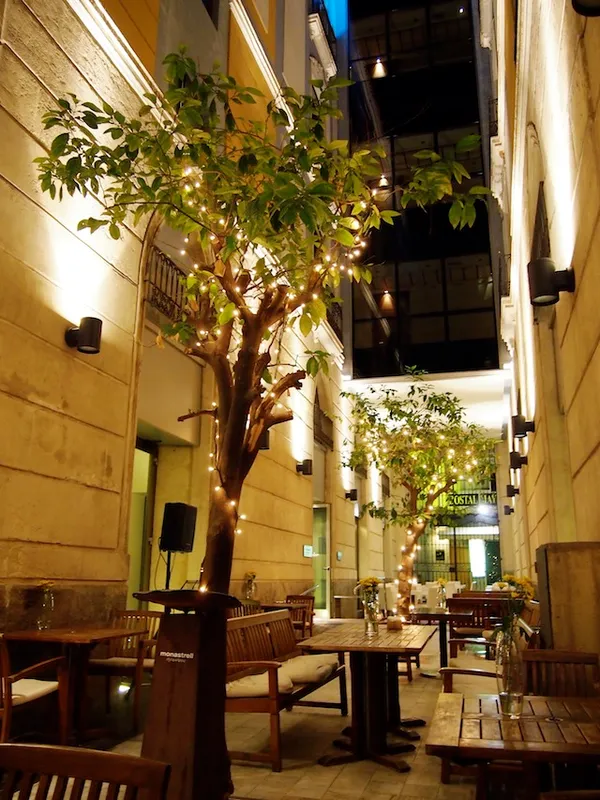 Evening terrace of Monastrell restaurant in Alicante with illuminated trees and branded podium sign