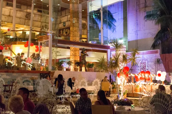 Candlelit outdoor courtyard of La Habichuela restaurant, Cancún, with ornate white iron chairs and Mayan statues