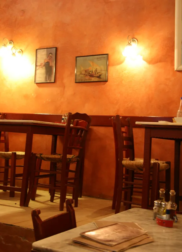 Interior of Tamam Restaurant, Chania, showing warm terracotta walls, marble tables and wooden chairs