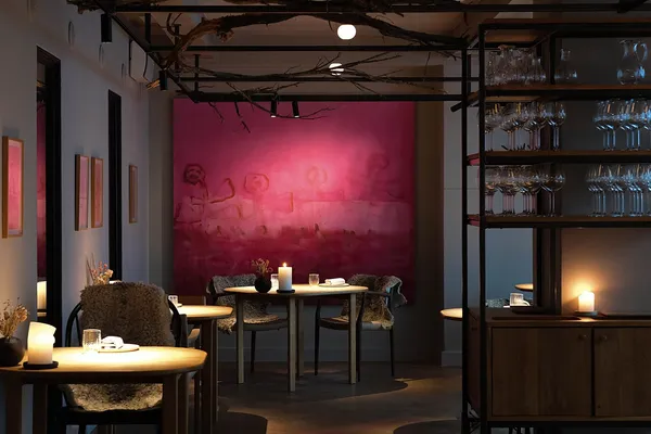 Kadeau Copenhagen dining room interior with candlelit tables, sheepskin chairs, and large pink artwork