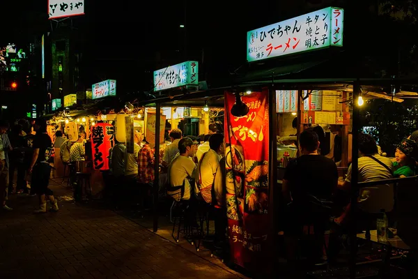Nakasu yatai outdoor food stalls lit up at night in Fukuoka with diners at the counter