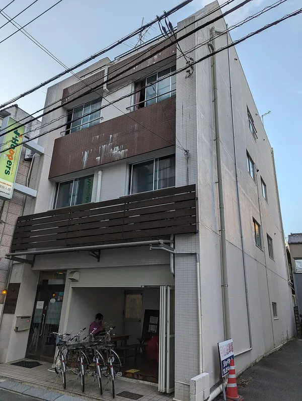 Exterior of J-Hoppers Hiroshima Guesthouse showing the green J-Hoppers sign on a multi-storey building
