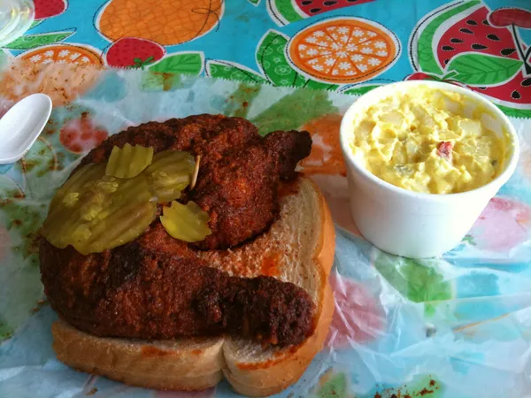 Nashville hot chicken on white bread with pickle slices and a side of potato salad