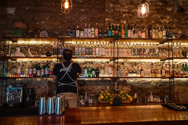 Interior of Sabina Sabe cocktail bar with backlit bottle shelves and stone walls, Oaxaca
