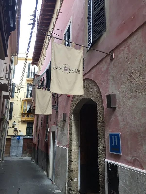 Exterior of Hotel Palau Sa Font in Palma de Mallorca, pink facade with hotel name banner and stone archway entrance