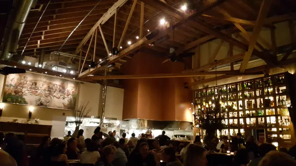Interior of Nostrana restaurant showing vaulted wood-beam ceiling, wine wall, and open kitchen