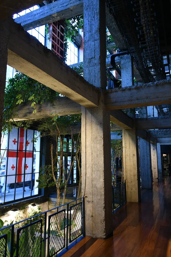 Stamba Hotel interior with raw concrete columns, indoor greenery and Georgian flag