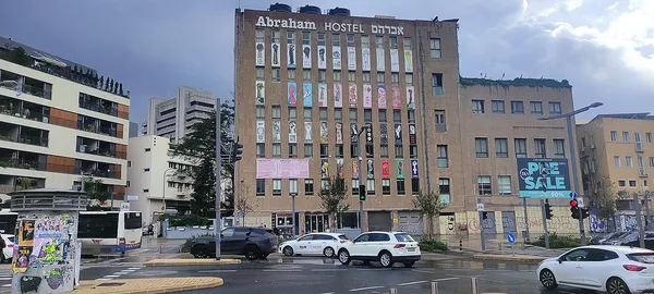 Exterior facade of Abraham Hostel Tel Aviv showing the large 'Abraham HOSTEL' sign in English and Hebrew with colourful banners