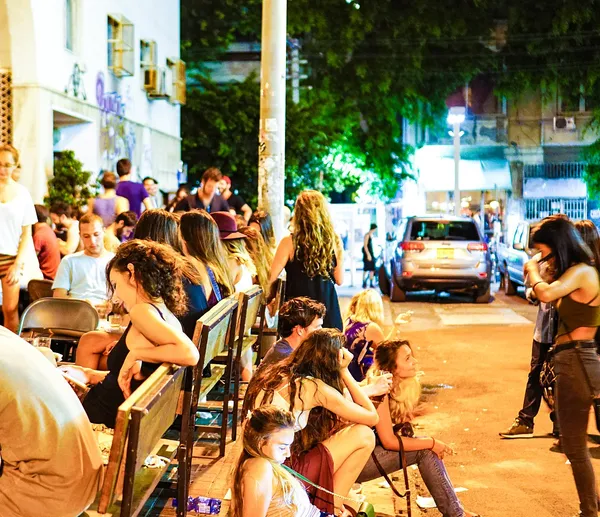 Crowded outdoor terrace of Port Said restaurant in Tel Aviv at night, with a large portrait mural on the building facade