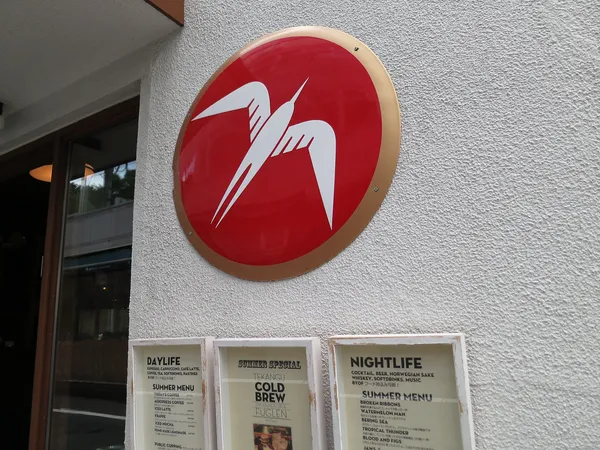 Exterior wall of Fuglen Tokyo coffee shop with red circular bird logo and menu boards