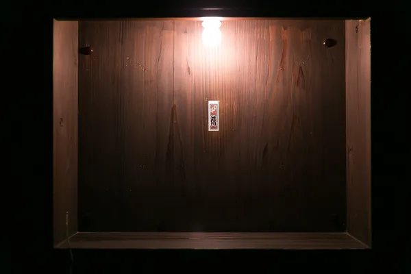 Dark wooden entrance door of Jimbocho Den restaurant with small nameplate sign illuminated by single overhead bulb